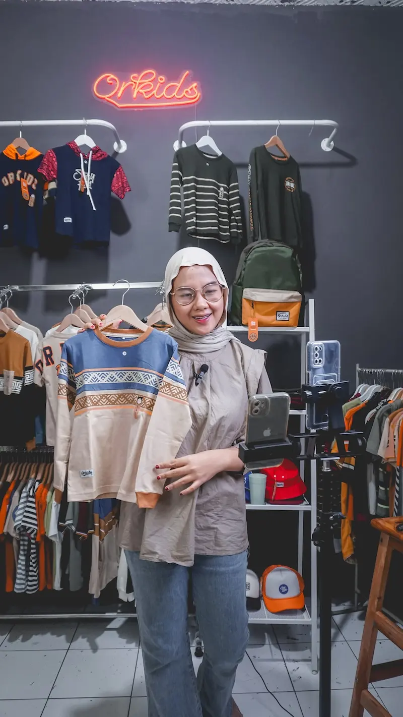 Host menunjukkan atasan pada hanger di studio dengan rak pakaian.
