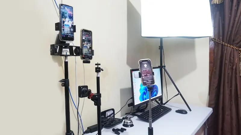 Meja siaran dengan ponsel pada penyangga, monitor, dan lampu studio.